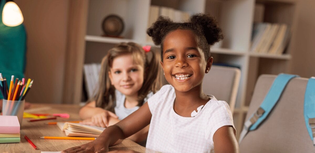 Deux enfants assis à une table, les mains posées sur le bureau, se livrent ensemble à une activité ciblée.