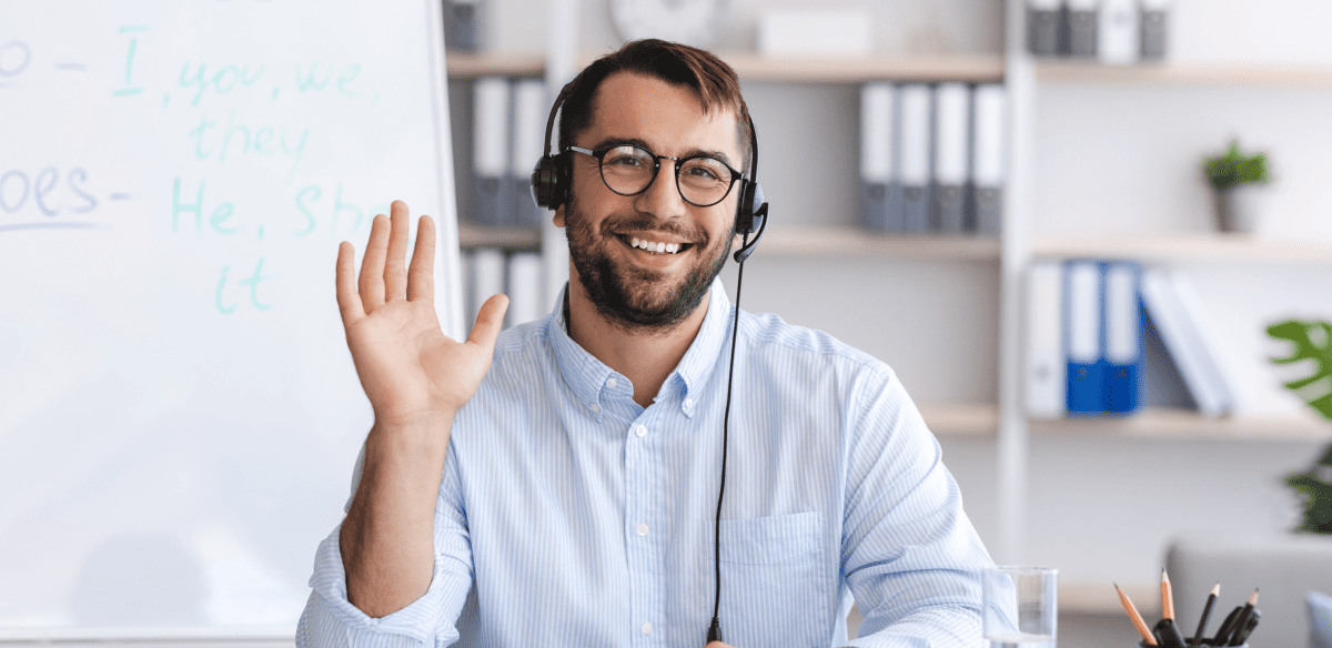 Un homme souriant, vêtu d'une chemise bleue et portant des lunettes, est assis à un bureau et lève les mains en signe d'excitation ou de célébration.