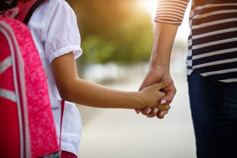 Une femme tient doucement la main d'un enfant, symbolisant l'amour et la connexion entre eux.