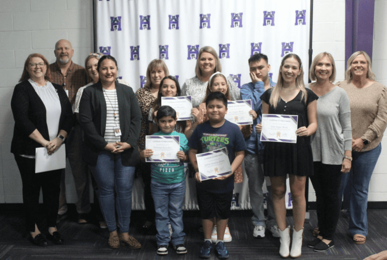 Un groupe diversifié de personnes affichant fièrement leurs certificats devant un mur violet vibrant.