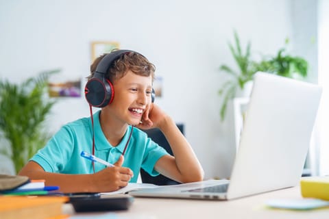 Un garçon avec des écouteurs est assis à un bureau, concentré sur son ordinateur portable, plongé dans son travail ou son divertissement.