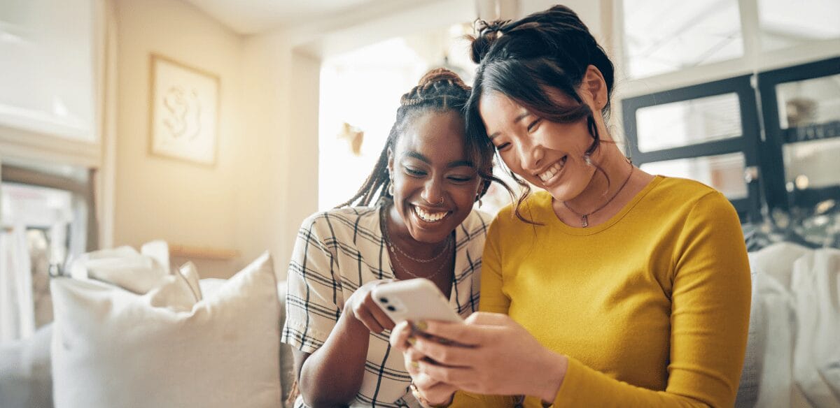 Deux femmes souriant et s'amusant avec leurs téléphones portables, partageant un moment de joie ensemble.