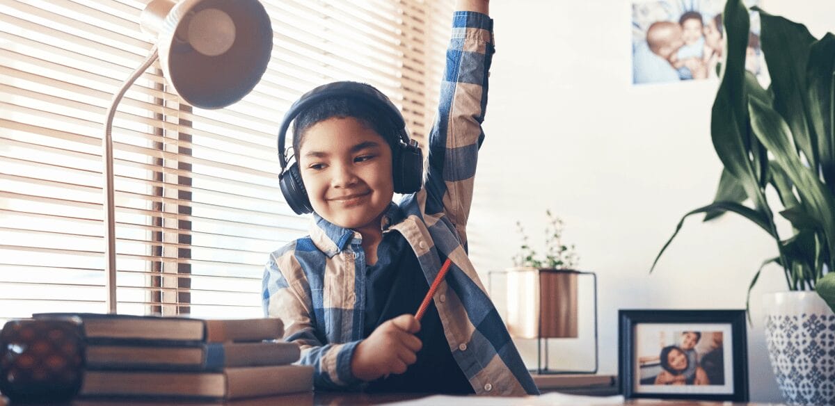 Un garçon portant des écouteurs est assis à un bureau, concentré sur son ordinateur portable, plongé dans son travail ou son divertissement.