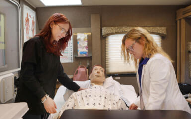 Deux étudiants en soins de santé s'exercent à soigner un patient sur un mannequin d'entraînement médical dans un laboratoire de simulation.