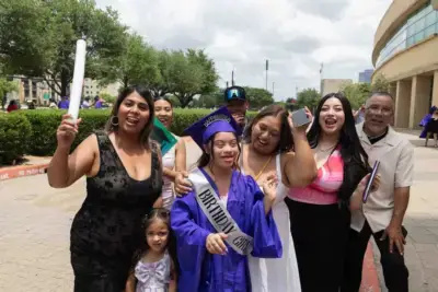 Heureuse diplômée coiffée d'un bonnet et d'une toge violets, portant une écharpe "Birthday Girl", entourée d'une famille joyeuse tenant un diplôme. Fête en plein air, journée ensoleillée.