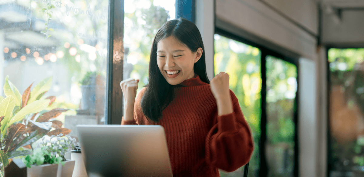 Une femme sourit tout en travaillant sur son ordinateur portable, illustrant un moment de joie et de productivité.